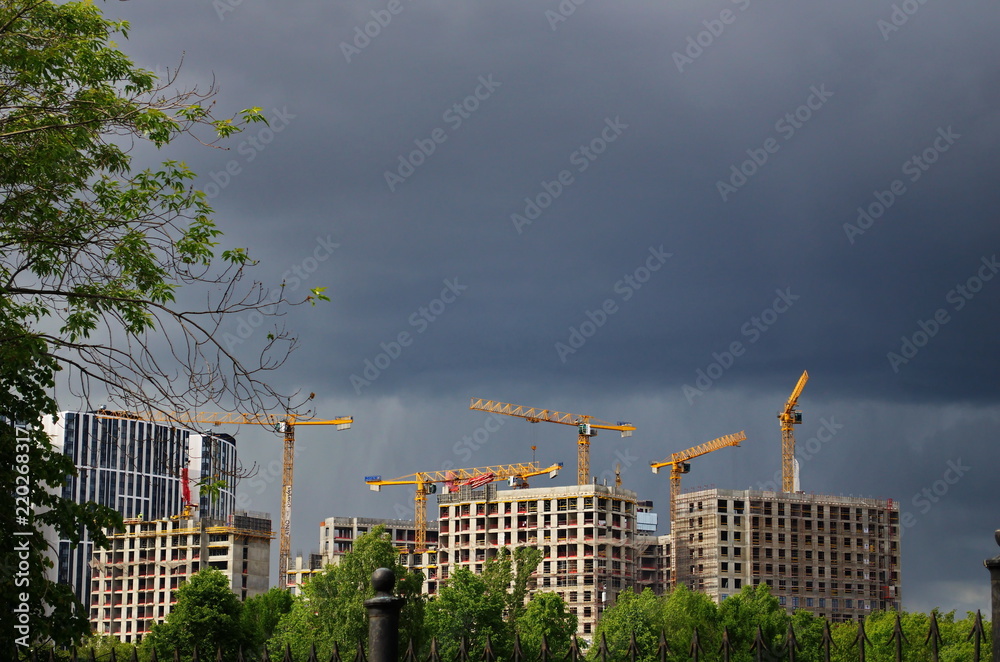 Houses under construction with tower cranes against the backdrop of a stormy sky Houses under construction with tower cranes against the backdrop of a stormy sky