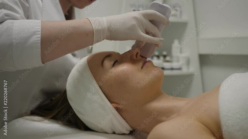 Cosmetologist makes an ultrasonic cavitation face peeling for young woman Cosmetologist makes an ultrasonic cavitation face peeling for young woman