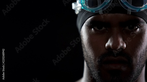 Masculine Hispanic swimmer wearing goggles, looking directly into camera, sport