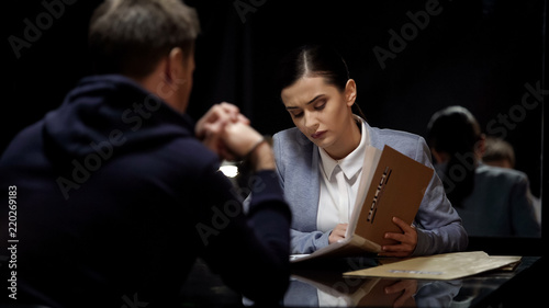 Young female police officer comparing suspect statements with file documents photo