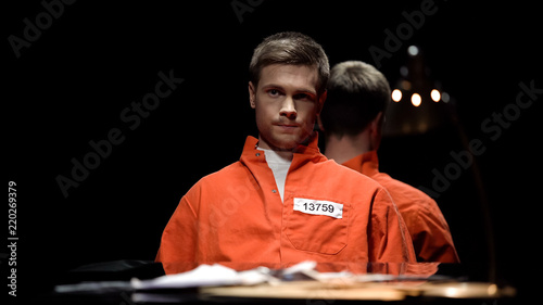 Valokuva Prime suspect in orange prison jumpsuit waiting for detective in police office