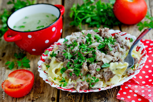 Beshbarmak national kazakh dish - egg noodles with boiled meat, onion and cilantro greens served with broth in bowl on wooden table photo