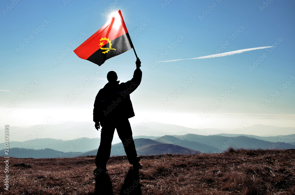 Successful silhouette man winner waving Angola flag on top of the mountain peak - obrazy, fototapety, plakaty 