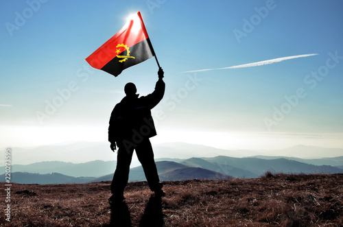 Successful silhouette man winner waving Angola flag on top of the mountain peak photo