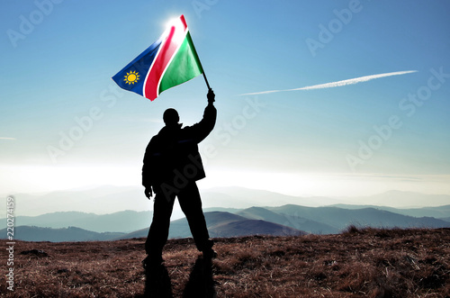 Successful silhouette man winner waving Namibia flag on top of the mountain peak photo