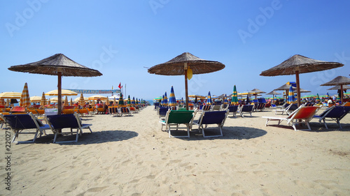 Summer beach resort bar lounge area with wooden easy chairs and straw parasols lined up next to the sea water