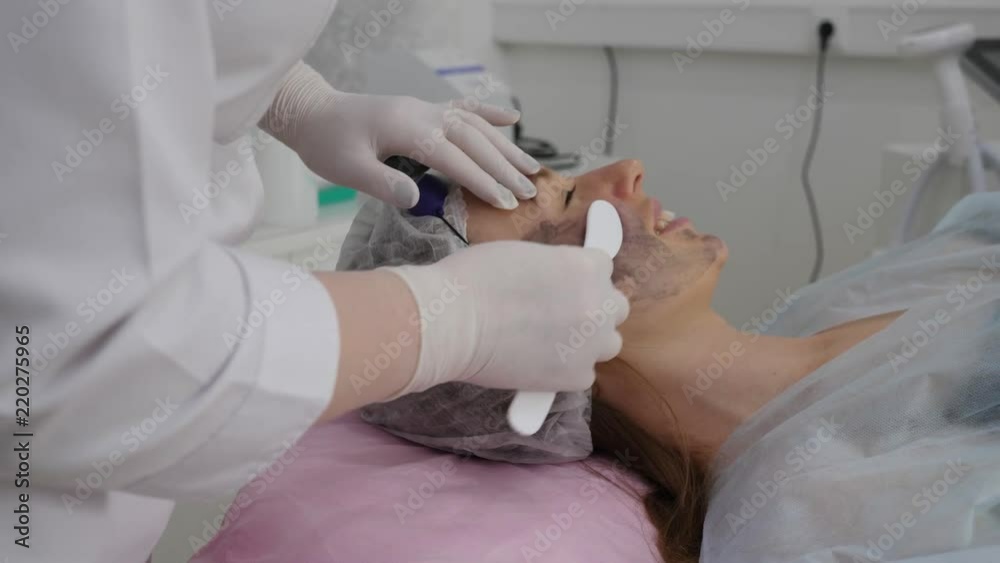 Cosmetologist applies cosmetic on woman's face for carbon peeling treatment Cosmetologist applies cosmetic on woman's face for carbon peeling treatment