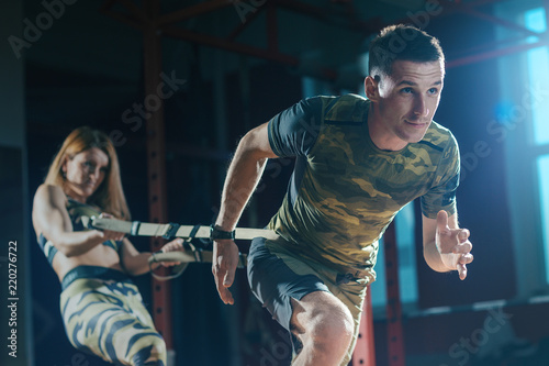 Sports training couple in the gym. Young man and woman doing exercise with rope trx system. Man pulls the ropes and woman holds her. Workout.