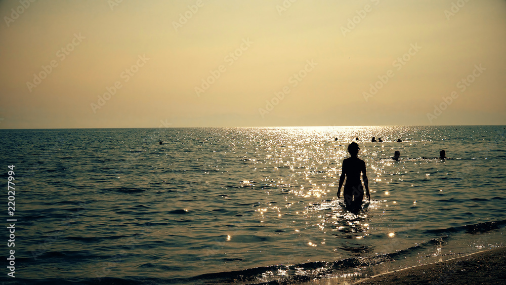 Surfer girl walking on beach into sea at sunrise, sunset
