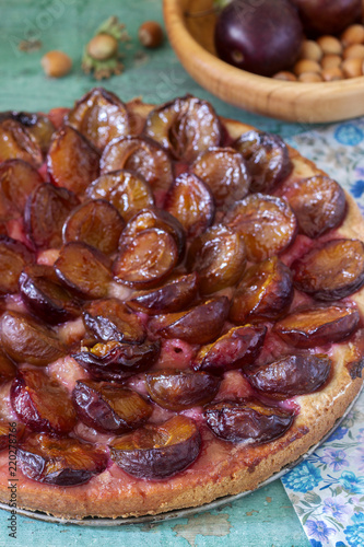 Sweet pie from short pastry with caramelized plums and ripe plums on a wooden table. Rustic style.