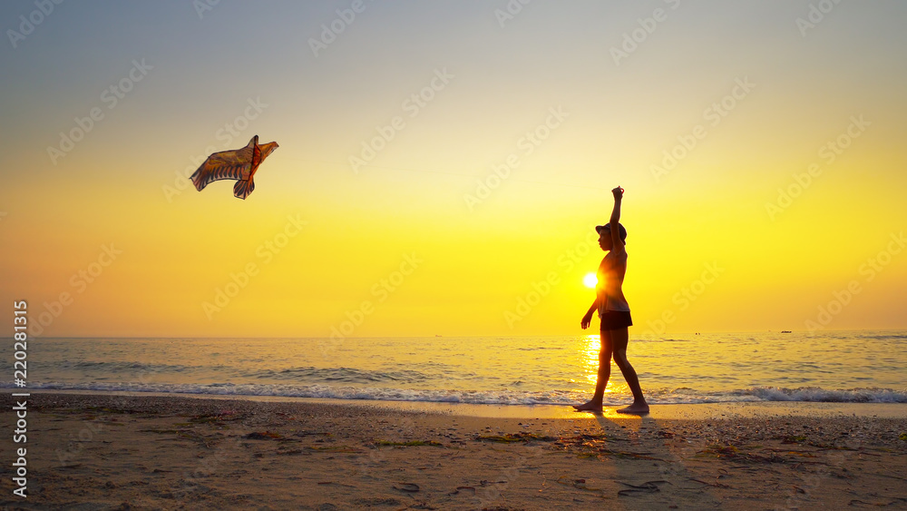 Summer vacation concept. Young boy running with kite on empty beach at sunset