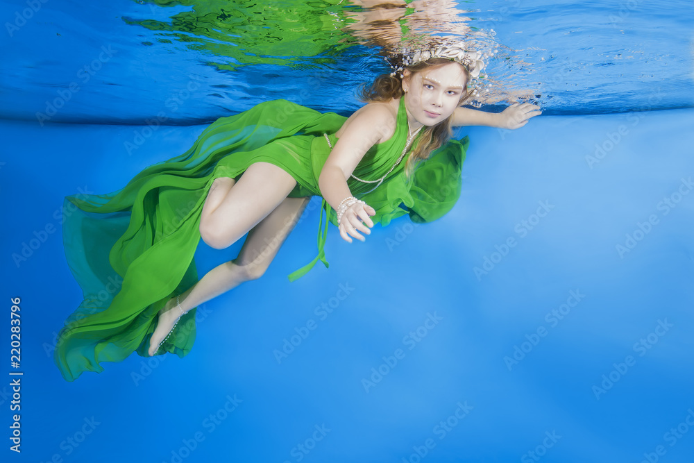 Girl in long, green dresses wearing poses underwater 