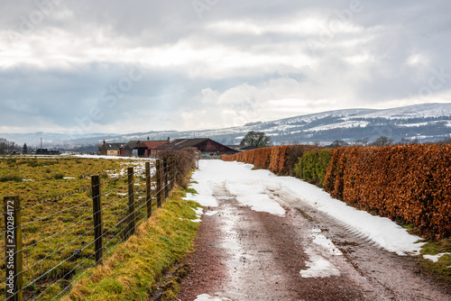 Narrow Driveway to a Farm Partially Covered in Melting Snow in the Scottish Highlands on a Cloudy Winter Day © alpegor