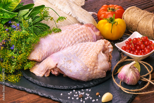 Raw chicken legs on a slate stone plate with spices, colorful tomatoes and red currant on a wooden rustic background. photo