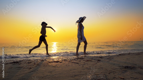 Tourism and travel vacation. Adorable family having fun on beach against sunset. Mother and son walk on beach an play, cinematic steadicam shot