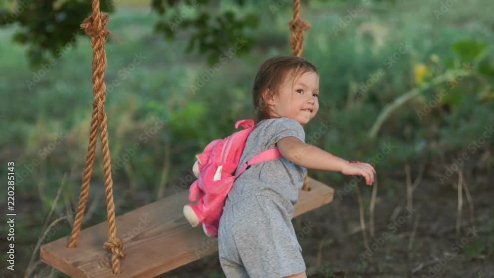 A little girl with a backpack on her back came to ride one on a swing. Summer holidays A little girl with a backpack on her back came to ride one on a swing. Summer holidays
