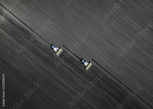 Aerial view of two blue tractors plows the earth in field on a summer day against a black earth background. Agriculture. Top view. Pattern