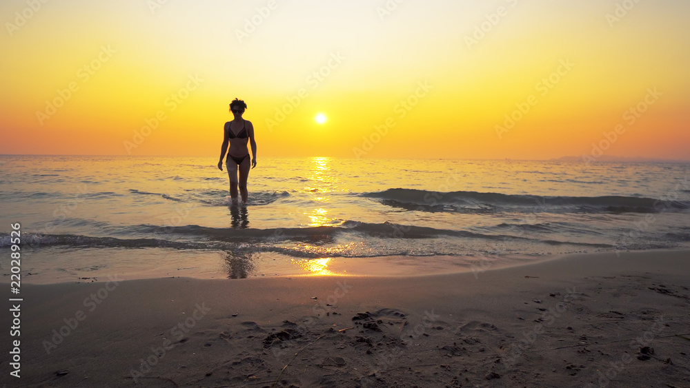 Naklejka premium Sexy fit fashion model go out of sea water with vibrant summer sunset at background