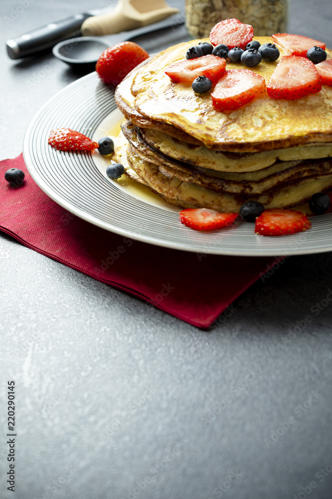 Sweet pancakes with honey, strawberries, and blueberry on a modern white plate. Sweet pancakes with honey, strawberries, and blueberry on a modern white plate.