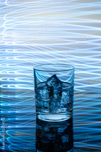 A glass beaker with a drink with ice on a colored background.