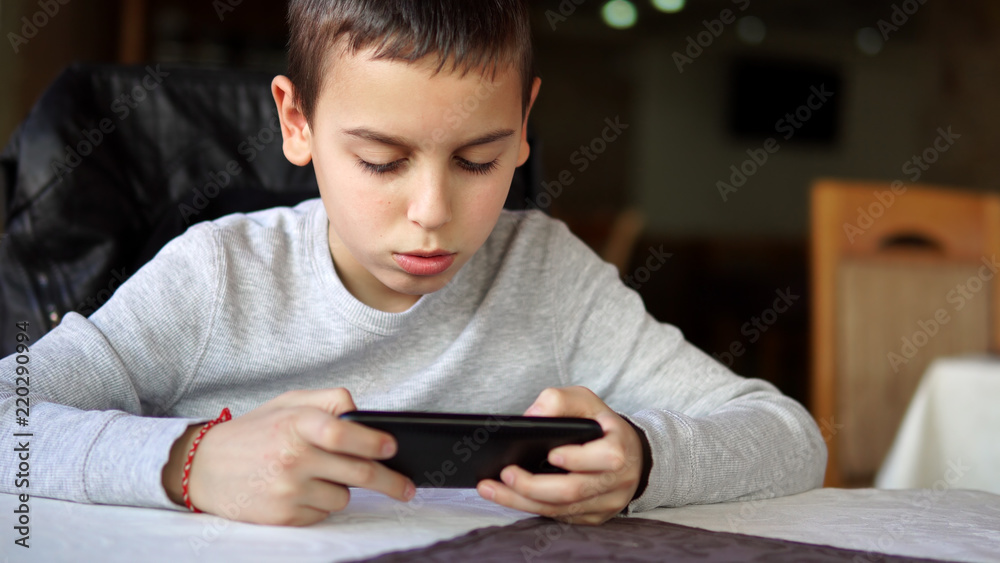 Little smiling child boy playing games or surfing internet on digital smartphone computer in cafe, cinematic dof Little smiling child boy playing games or surfing internet on digital smartphone computer in cafe, cinematic dof
