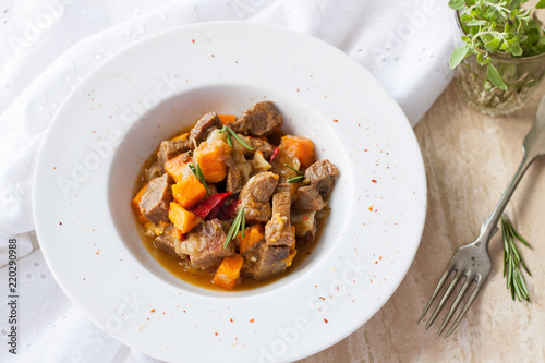 Beef stew with butternut squash, pepper and onion decorated with fresh rosemary in white plate on marble table