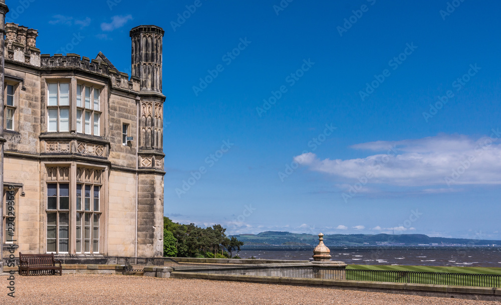 Edinburgh, Scotland, UK - June 14, 2012: Corner of Dalmany house, mansion and castle in Tudor revival style and Firth of Forth in back. Blue sky.