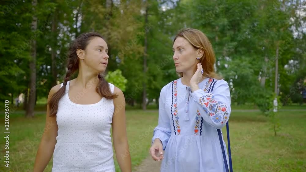 two adult relaxed women are walking slowly in park and chatting, gossiping and discussing two adult relaxed women are walking slowly in park and chatting, gossiping and discussing