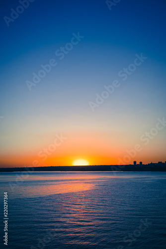 Sunset view from the Paranoa lake in Brasilia near by JK Bridge. In this photo: blue sky, orange and vivid sunset, blue lake without motion. © Thi Soares