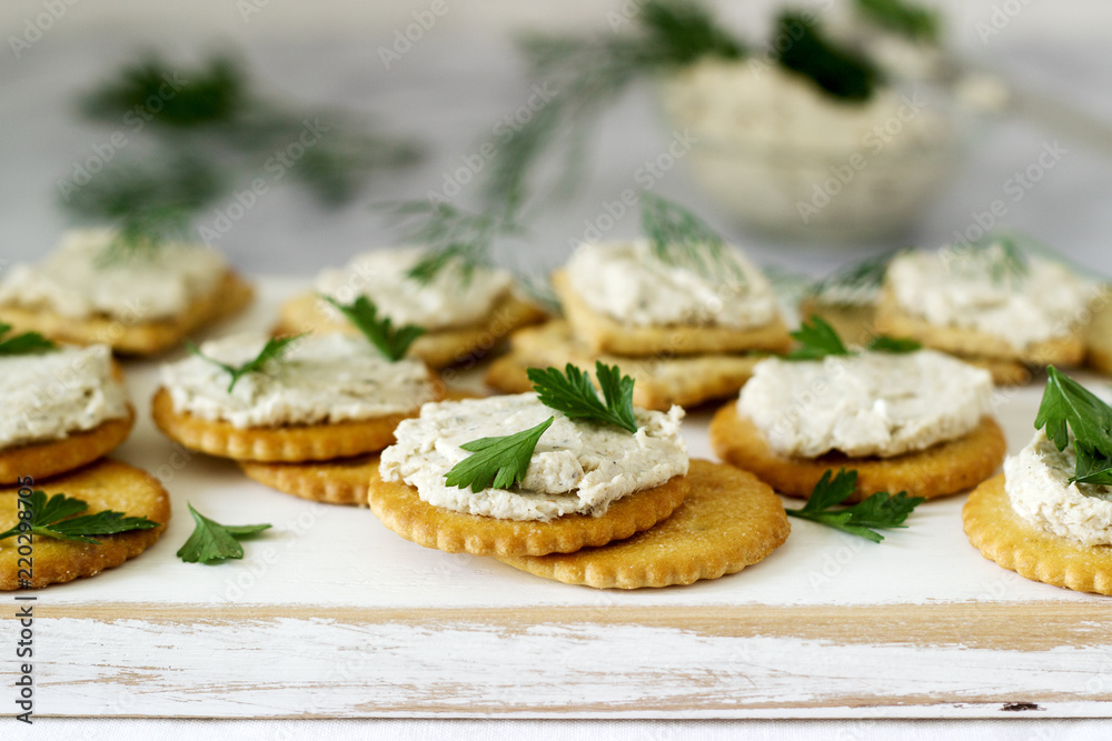 Snack from crackers and curd fish paste with herbs on a light background.