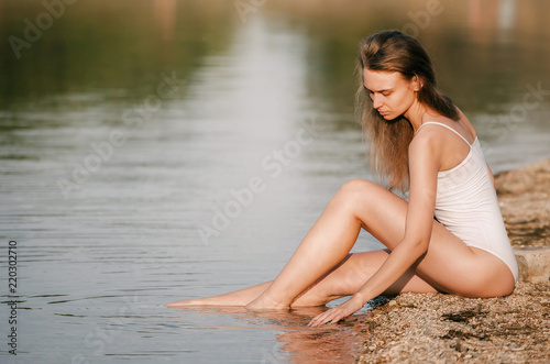 Beautiful young sexy girl in a swimsuit sunbathing on the beach, sitting by the sea, leaning on a stone