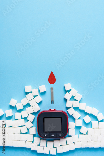 red blood drop and wall made of sugar cubes ruined by Blood glucose test strips and Glucose meter on blue background