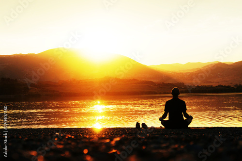 Silhouette of a man meditating on the shore at sunset
