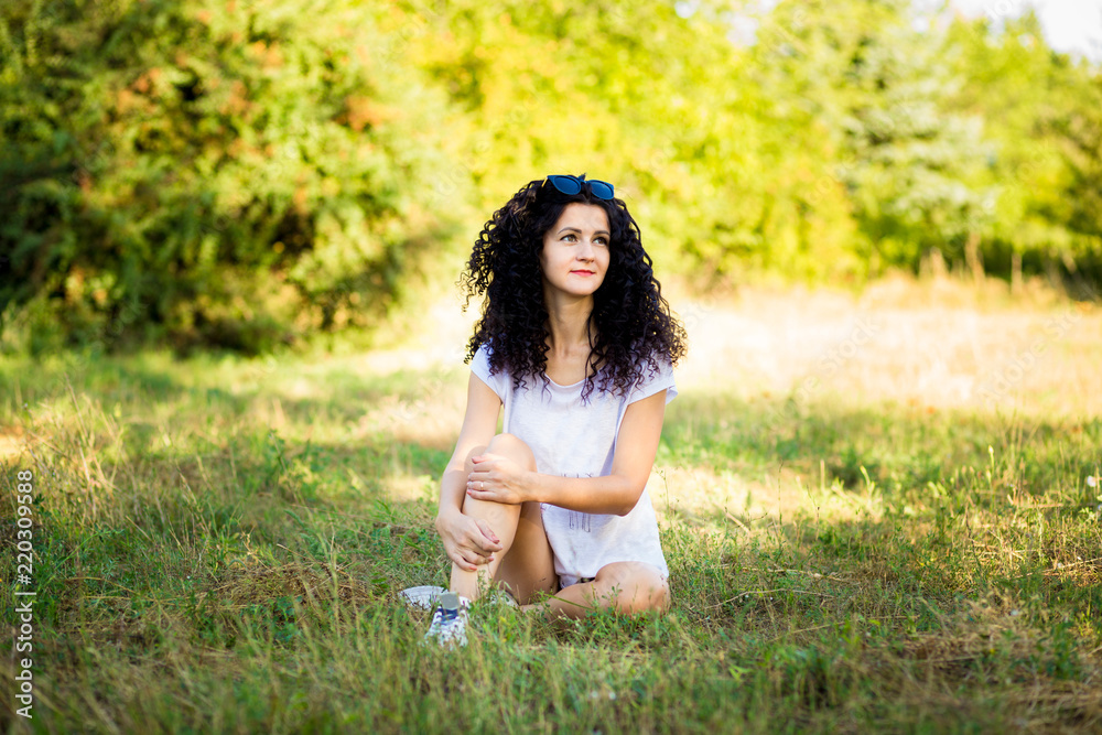 Pretty curly woman posing on grass in sunny day Pretty curly woman posing on grass in sunny day