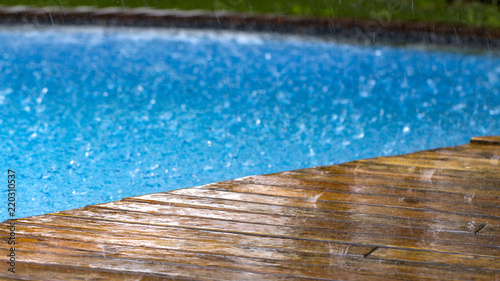 drops of rain fall on a wooden terrace and a bridge near the pool photo