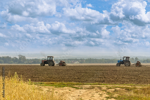 Beautiful agricultural landscape under the cloudy sky - two old tractors equipped with seeders. Farmers sowing winter wheat in autumn