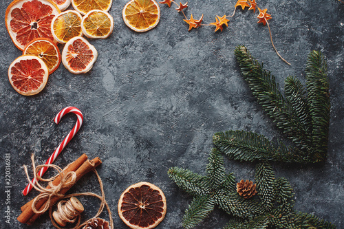Christmas or New Year flat lay home decor, dry oranges, cinnamon, candies and fir branches on concrete background. Cozy winter homely scene, top view, copy space