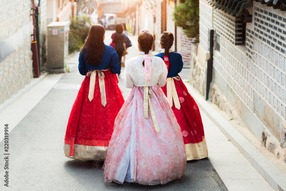 Fototapeta premium Tył trzech kobiet w hanbokach spacerujących po tradycyjnych domach w wiosce Bukchon Hanok w Seulu w Korei Południowej.