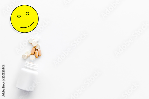 Reception of medicines concept. Recovery. Pills falling out of jar near smile face emoji on white background top view copy space