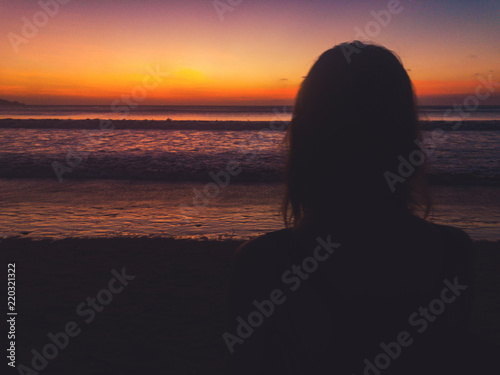 Lonely girl looking at the ocean / sea view at sunset time. Optical focus is on the ocean.