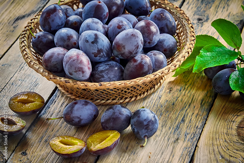 Fresh plums with leaves in basket on wooden background