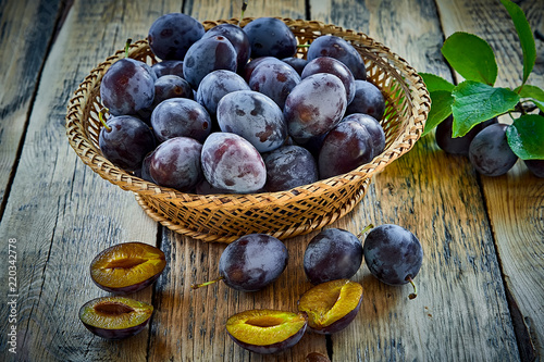 Fresh plums with leaves in basket on wooden background