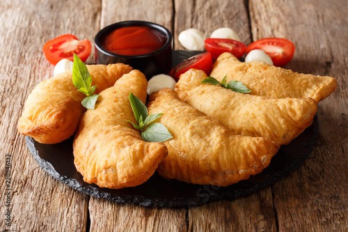 Hot fried panzerotti with a filling of tomatoes, herbs and mozzarella close-up are served on a board. horizontal