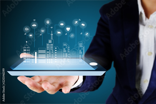 Businessman holding a digital smart phone or tablet with a digital smart city and smart service icon , internet of things concept..