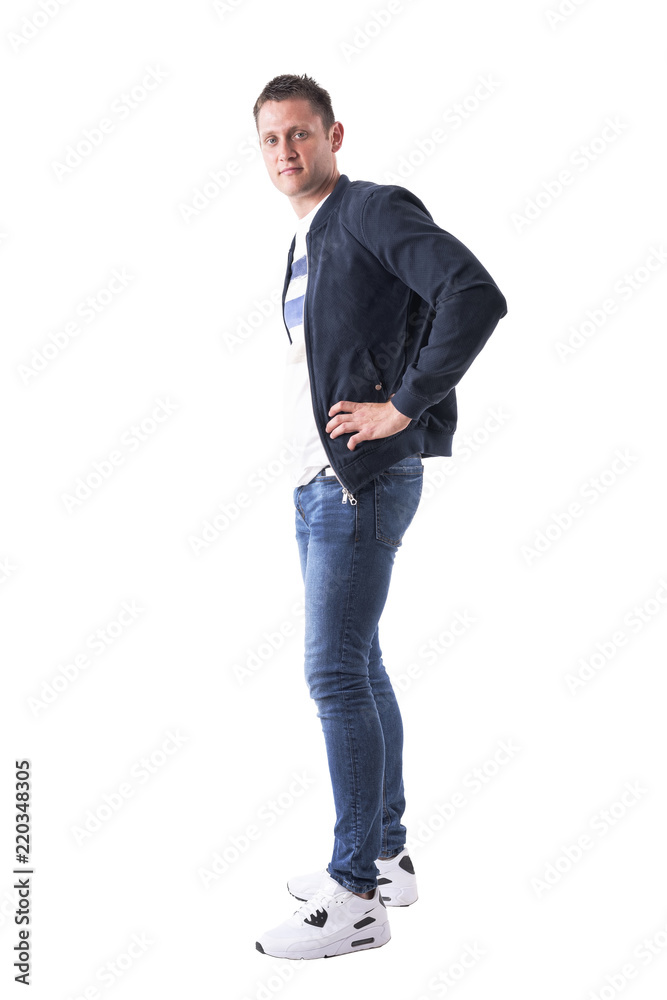 Side view of relaxed confident man with hands on hips in bomber jacket looking at camera. Full body isolated on white background. Side view of relaxed confident man with hands on hips in bomber jacket looking at camera. Full body isolated on white background.