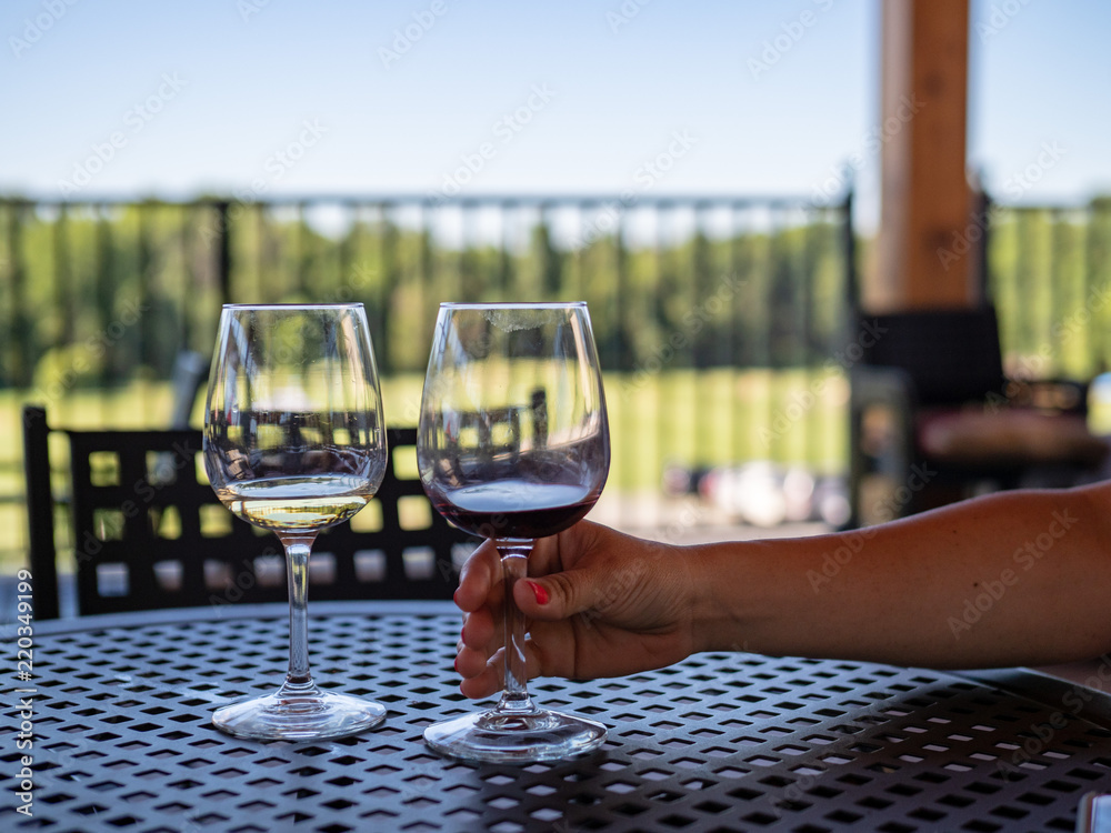 Woman's arm reaching for almost empty glasses of red and white wine on an outdoor patio table