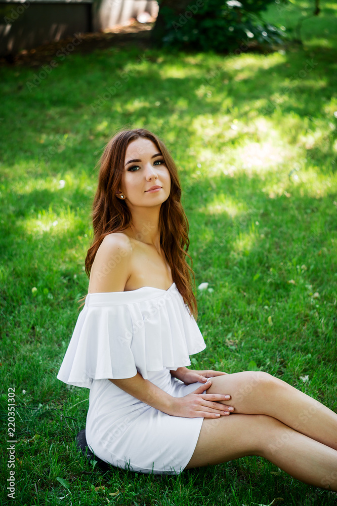 A young woman in a white dress sitting in the park on the road.