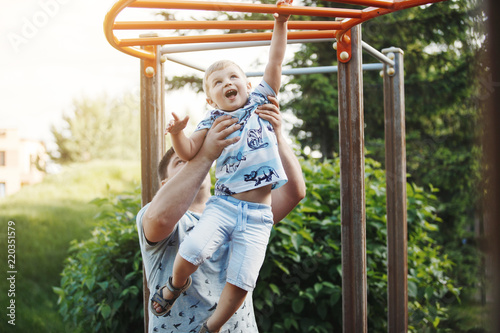 Young father and a blond boy in blue T-shirts climb the stairs at the children's playground in the summer.