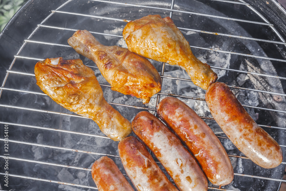 .Grilled sausages and chicken legs close-up on the grill. .Delicious.tasty juicy roast meat. Cooking food outdoor.