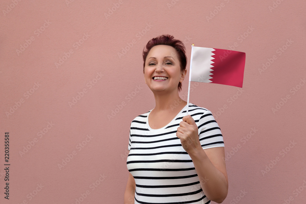 Qatar flag. Woman holding Qatar flag. Nice portrait of middle aged lady 40 50 years old with a national flag over pink wall background outdoors. Qatar flag. Woman holding Qatar flag. Nice portrait of middle aged lady 40 50 years old with a national flag over pink wall background outdoors.